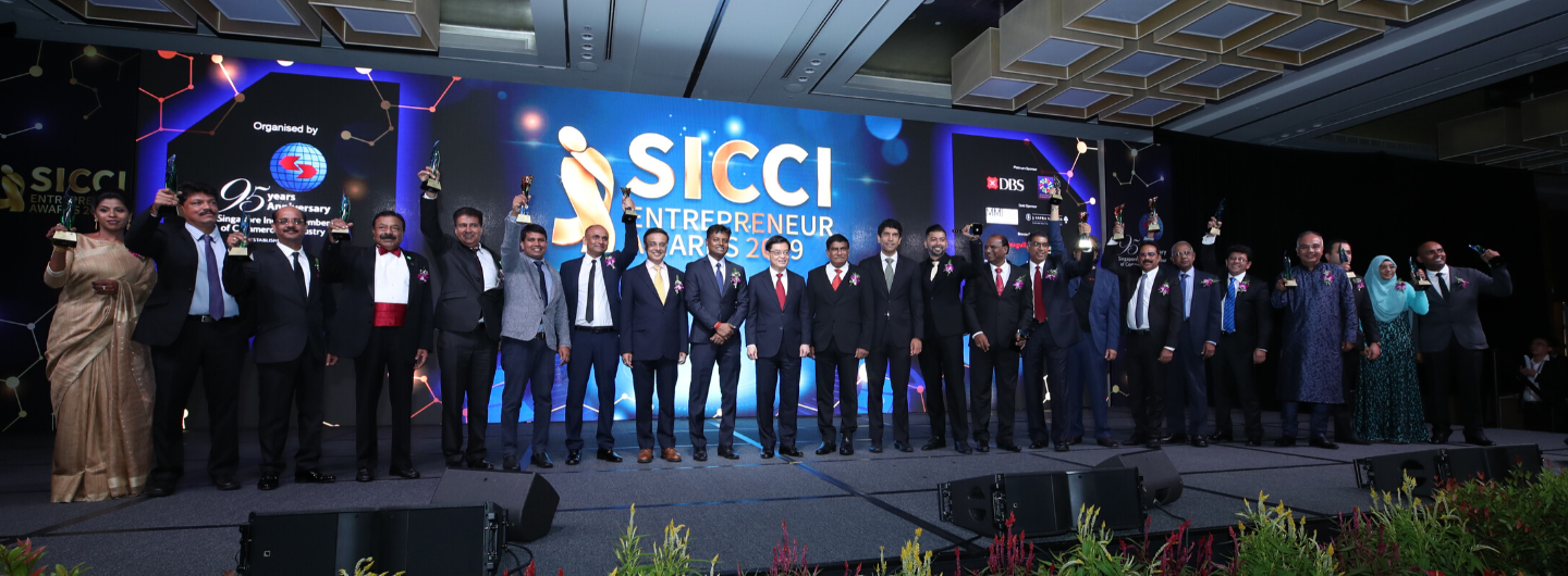 Group of people in formal attire holding awards onstage at a SICCI event.